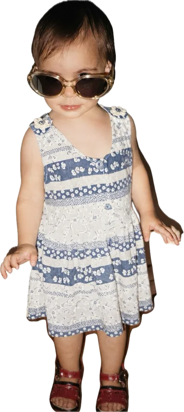 Elene as a little girl, in sunglasses and a summer dress